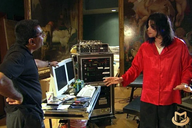 Imagen del ingeniero Michael Jackson parado frente a uno de sus asistentes explicandole en detalle lo que harán, detrás hay unos computadores, cables y circuitos del proyecto que están desarrollando
